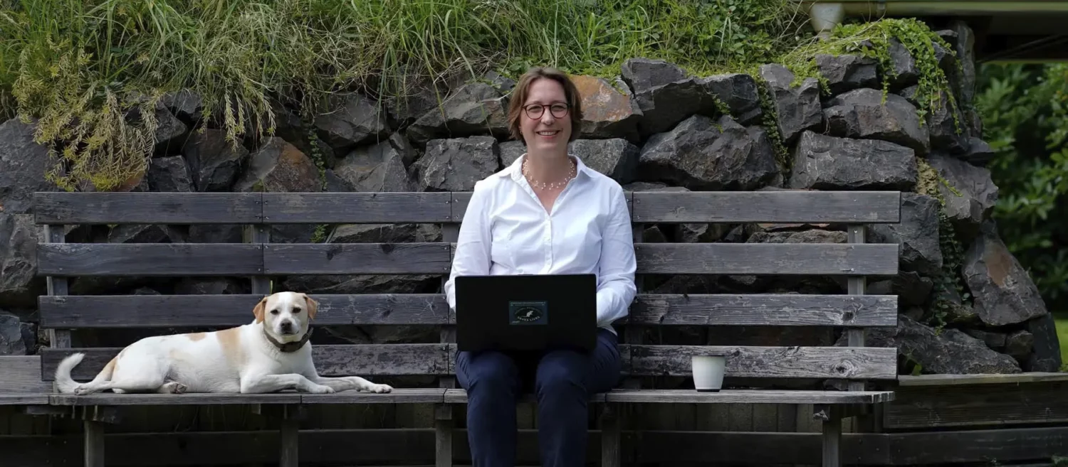 Stefanie Flunkert mit ihrem Hund und Laptop auf einer Garten-Bank